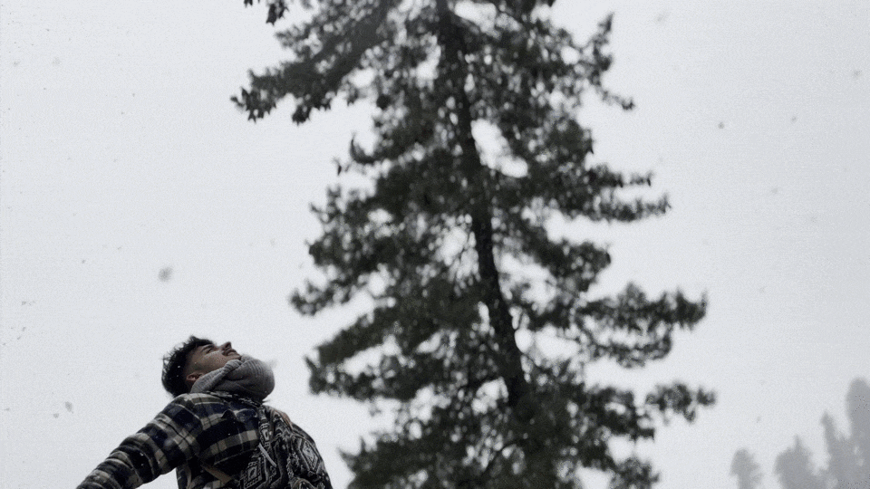 A person looking up and clapping while snow falls